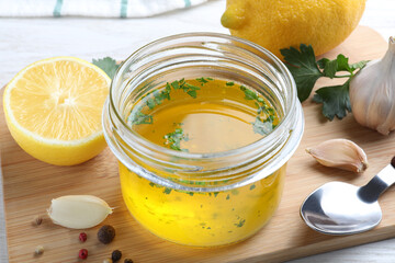 Jar with lemon sauce and ingredients on wooden board, closeup. Delicious salad dressing