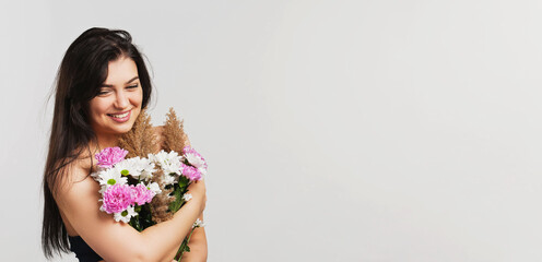 Smiling beautiful pretty lady brunette holds bunch of lovely flowers hiding her breasts on white background.