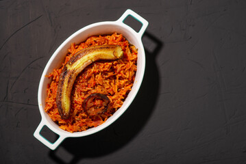 Jollof rice with fried banana. Traditional Nigerian rice food with tomatoes, onions and spices. Dark background. Place for text.