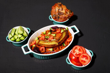 Jollof rice with fried banana, baked chicken. Rice with tomatoes, onions, spices. Traditional national Nigerian food. Dark background.