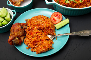 Jollof rice with chicken meat on a plate. Rice with tomatoes, onions, spices. Traditional national Nigerian food. Dark background.