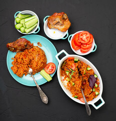 Jollof rice with chicken meat on a plate. Rice with tomatoes, onions, spices. Traditional national Nigerian food. Dark background.