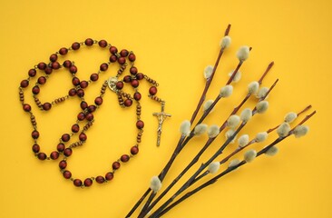 Dry willow branches and rosary wooden prayer beads crucifix on yellow background. Palm Sunday spring holiday. Holy week christian religious concept. Flatlay, lay out, top view