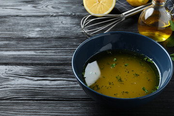 Bowl with lemon sauce on black wooden table, space for text. Delicious salad dressing