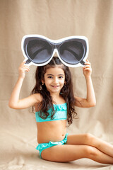 Funny little girl about 6 years old in a casual summer swimsuit posing on a plain beige background. The concept of a child's lifestyle. Layout of the copy space.