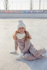 Funny little blonde girl of 7 years old in casual clothes posing on a skating rink in skates. The...