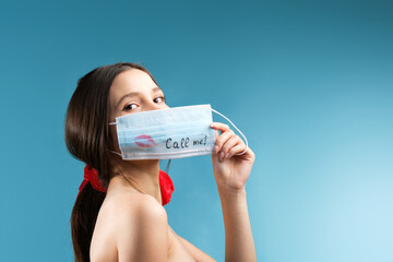 An attractive brunette girl in keeping the medical mask in a hand covering her face with a kiss sign and written call me.