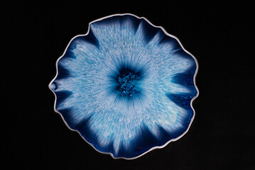 Plate with epoxy resin. Dish with blue and light blue stains on a black background