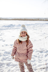 Funny little blonde girl of 7 years old in casual winter clothes posing outside in snowy weather . The concept of a child's lifestyle. Layout of the copy space.