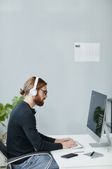 Contemporary young diversity programmer in casual clothes and headphones working in front of...