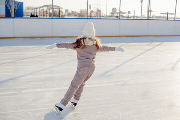 Funny little blonde girl of 7 years old in casual clothes posing on a skating rink in skates. The...