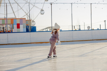 Funny little blonde girl of 7 years old in casual clothes posing on a skating rink in skates. The...