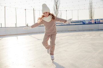 Funny little blonde girl of 7 years old in casual clothes posing on a skating rink in skates. The...