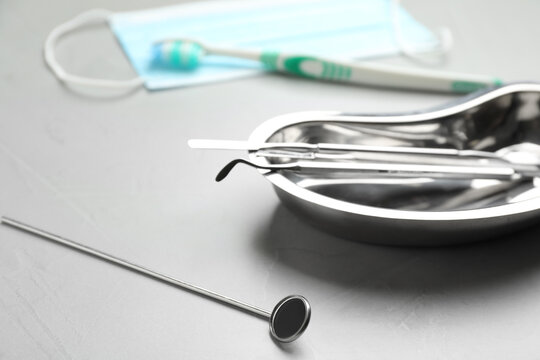 Mouth mirror near kidney shaped tray with dentist's tools on grey table, closeup