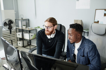 Two young intercultural diversity programmers looking at compute screen while developing new programs in openspace bureau