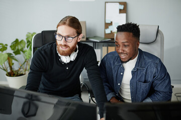 Small group of happy young intercultural diversity programmers in casual clothes working in front of computer monitors in office