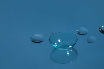 Contact lens and drops of water on blue reflective surface. Space for text