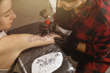 Process of drawing tattoo on arm, tattoo master dressed in medical gloves carefully drawing on skin...