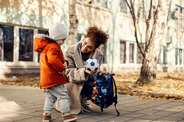 A nanny wants to play football or soccer with a little boy so she is showing him a ball.