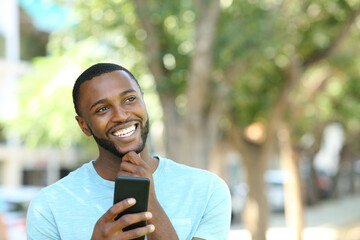 Happy man with black skin thinking holding phone