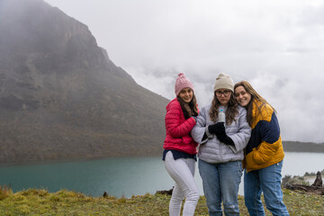 Three friends posing while facing the camera in front of a mountain lake