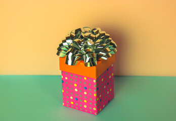 Pink gift box in multicolored polka dots with silver bow in center of photography on yellow and...