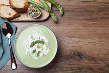 Delicious asparagus soup with pumpkin seeds served on wooden table, flat lay. Space for text