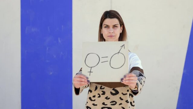Close-up of a young Caucasian woman on the street showing a cardboard with a symbol of gender equality drawn on it