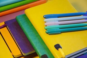 Bright notepads and colored pens on a background of colored paper. writing accessories. Corporate gifts for office employees. Sunny mood for work.