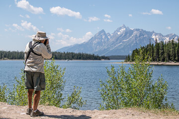A photographer taking a picture of a mountain by a lake
