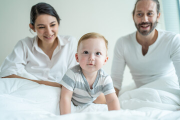 Caucasian parents play with cute baby boy child infant on bed at home. 