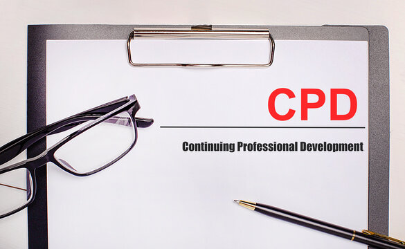 On a light wooden background glasses, a pen and a sheet of paper with the text CPD Continuing Professional Development. Business concept