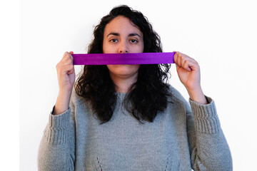 Young woman holds a purple ribbon between her hands covering her mouth on a white background....