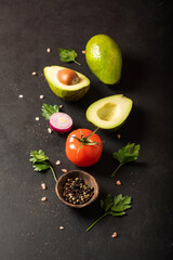 Fototapeta na wymiar Fresh ingredients for guacamole: avocado, tomato,red onion, cilantro on a black background. With space for text.