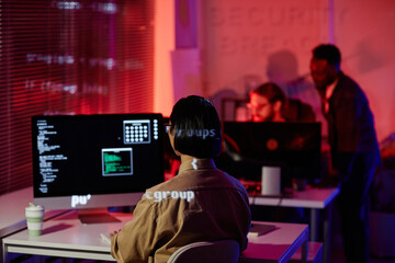 Obraz premium Rear view of young contemporary programmer sitting in front of computer screen with decoded data and working in openspace office