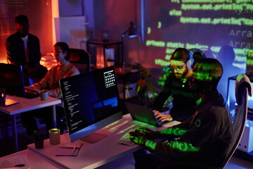 Group of young intercultural office workers sitting by desks in front of computers and decoding...
