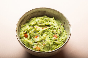 Traditional Mexican Guacamole sauce made from avocado. lime, red onion, tomatoes, cilantro on a pink background.