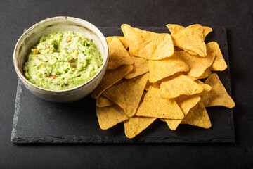 Mexican nachos chips and bowl with homemade fresh guacomole sauce made from avocado and lime  over...