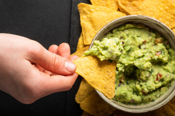 Young man hand is picking some guacamole dip with nachos chip. Healthy Vegan, Vegetables food.