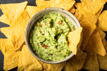 Mexican nachos chips and bowl with homemade fresh guacomole sauce made from avocado and lime  over black background. - obrazy, fototapety, plakaty