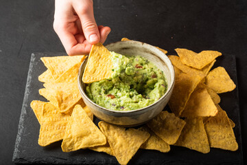 Young man hand is picking some guacamole dip with nachos chip. Healthy Vegan, Vegetables food.