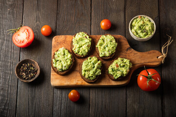 Sandwiches with guacamole sauce on a cutting board over old wooden background.