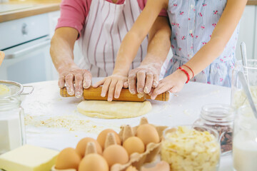 Child and grandmother in the kitchen bakes prepares the dough in the kitchen. Selective focus.