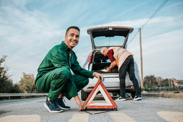 Two road assistant workers in towing service trying to fix car engine. One worker in foreground...