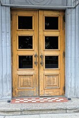 one old brown door made of wood and glass on a gray concrete wall of a historical building on the street