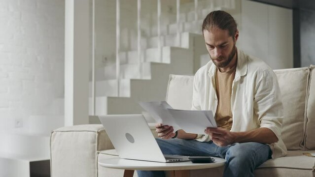 Handsome man doing paperwork while using laptop at home