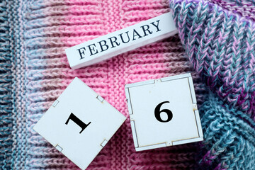 Calendar for February 16: cubes with the numbers 16, the name of the month of February in English on a multi-colored jersey, top view