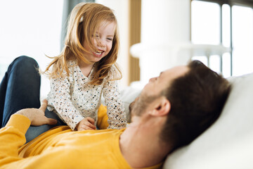 Young happy father having fun with his small girl on sofa at home