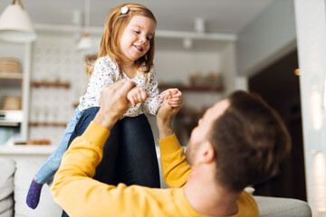 Young father having fun while playing with his little daughter on sofa at home.