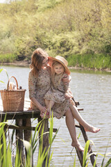 Mother and daughter in matching dress on the wooden pier. Nice idyllic family day in nature.